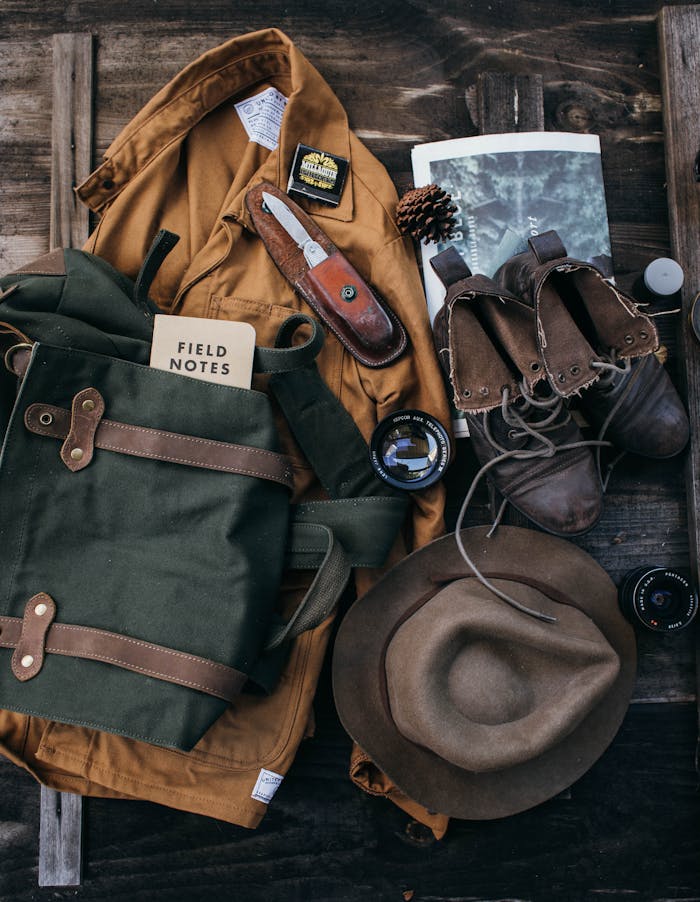 Home Top view of costume with hat and old fashioned boots placed on wooden surface with backpack and lens near newspaper